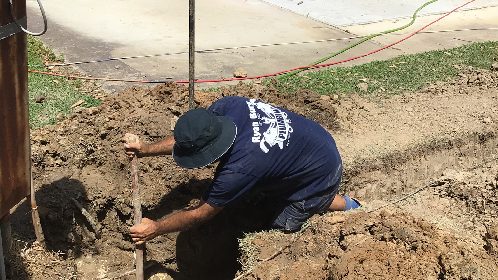 Ryan Bury Plumbing worker digging a trench by hand for a drainage repair