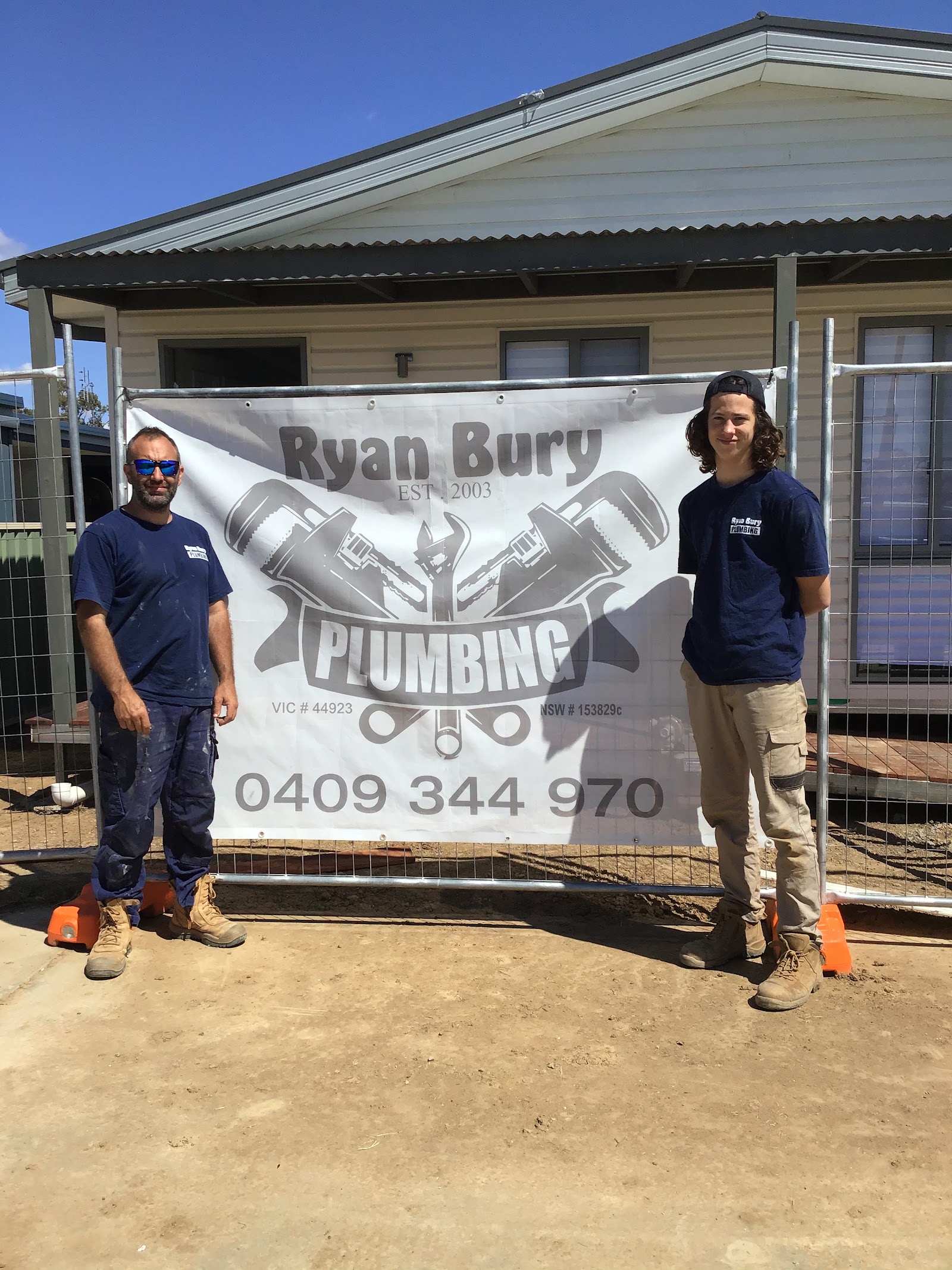 Ryan Bury Plumbing crew standing either side of the company banner at a job site